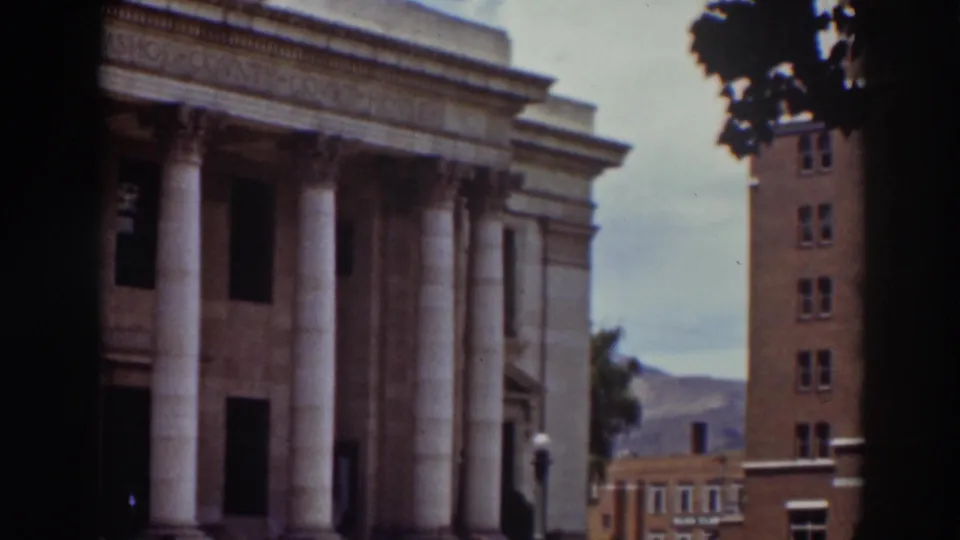 1937 Truckee home-movie frame showing a classical-columned building, nearby brick structure, and distant hills.