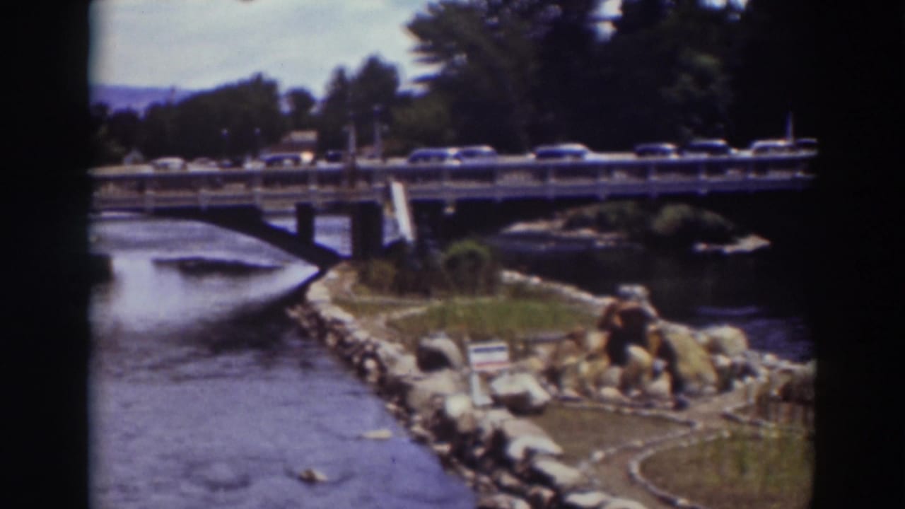 Cars travel across a Truckee bridge over moving water, with rocks, grass, trees, and hills visible in the 1937 frame.