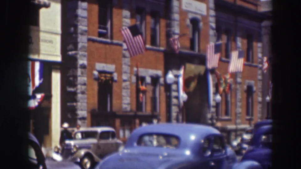 1937 Truckee street view showing a brick-and-stone building with American flags, striped awnings, and parked cars.