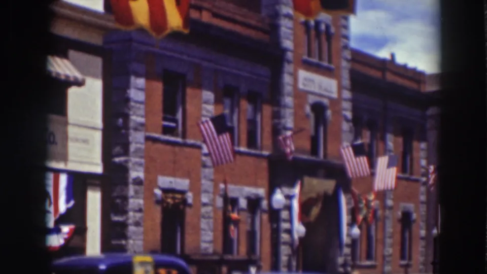 The 8mm frame shows a Truckee brick building with American flags, colorful banners, stone trim, and 1930s cars at the curb.