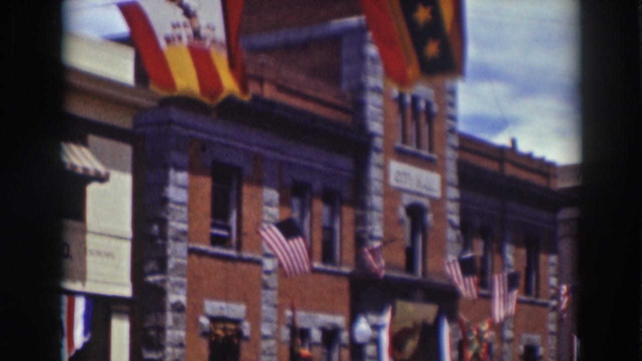 1937 Truckee street facade with American flags, awnings, upper windows, and a red-and-yellow banner above the storefronts.