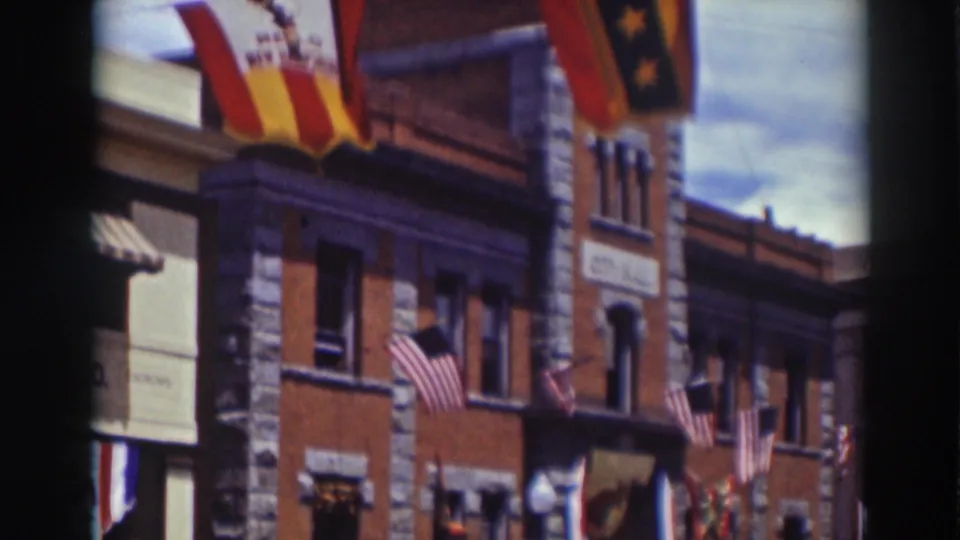 1937 Truckee street facade with American flags, awnings, upper windows, and a red-and-yellow banner above the storefronts.