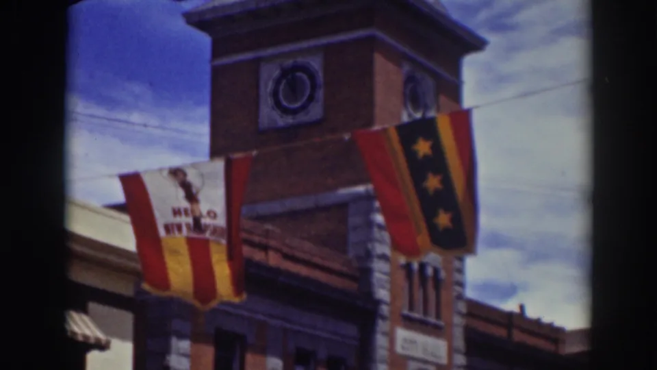 1937 Truckee, California 8mm frame showing a brick clock tower with a striped welcome banner and a dark star flag below a cloudy blue sky.