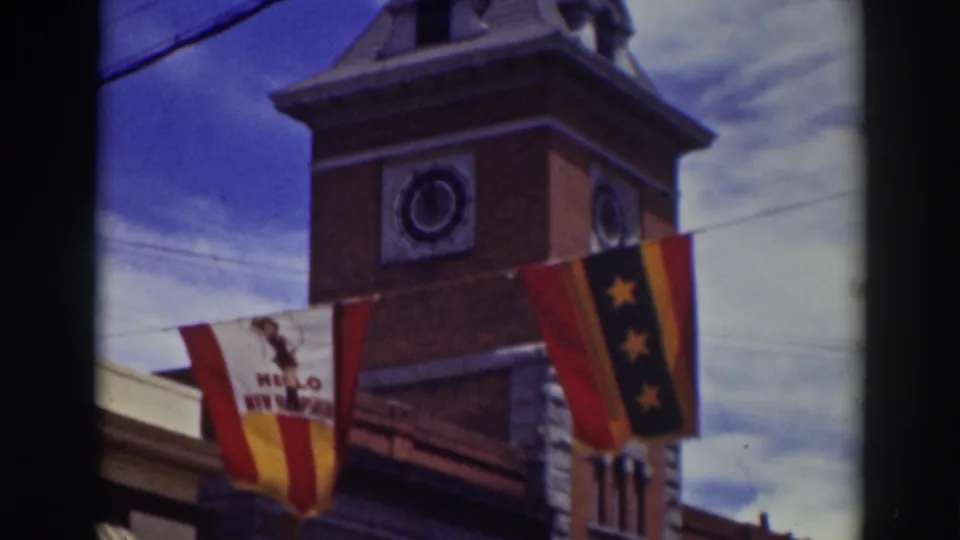 The clock tower remains framed from below, with the HELLO NEW HAMPSHIRE banner partly readable beside a dark flag with yellow stars.