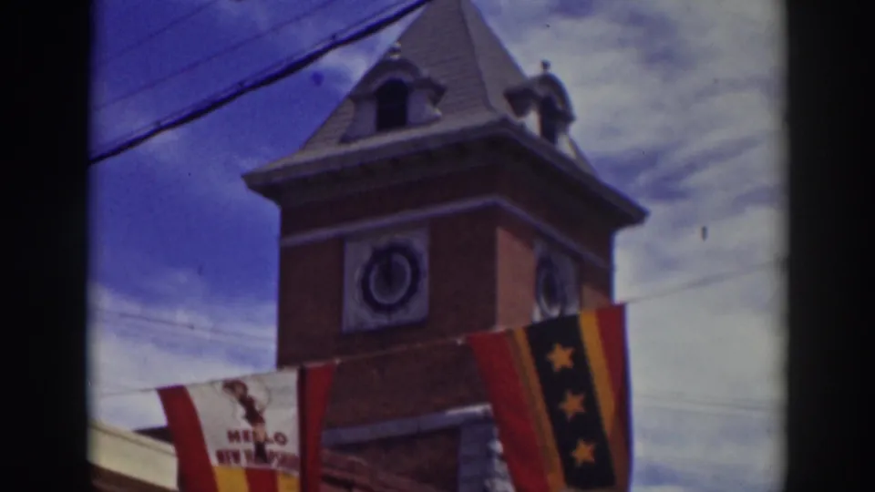 Upward 8mm view of the Truckee clock tower roof and clock face, with the striped banner and star flag crossing the lower frame.