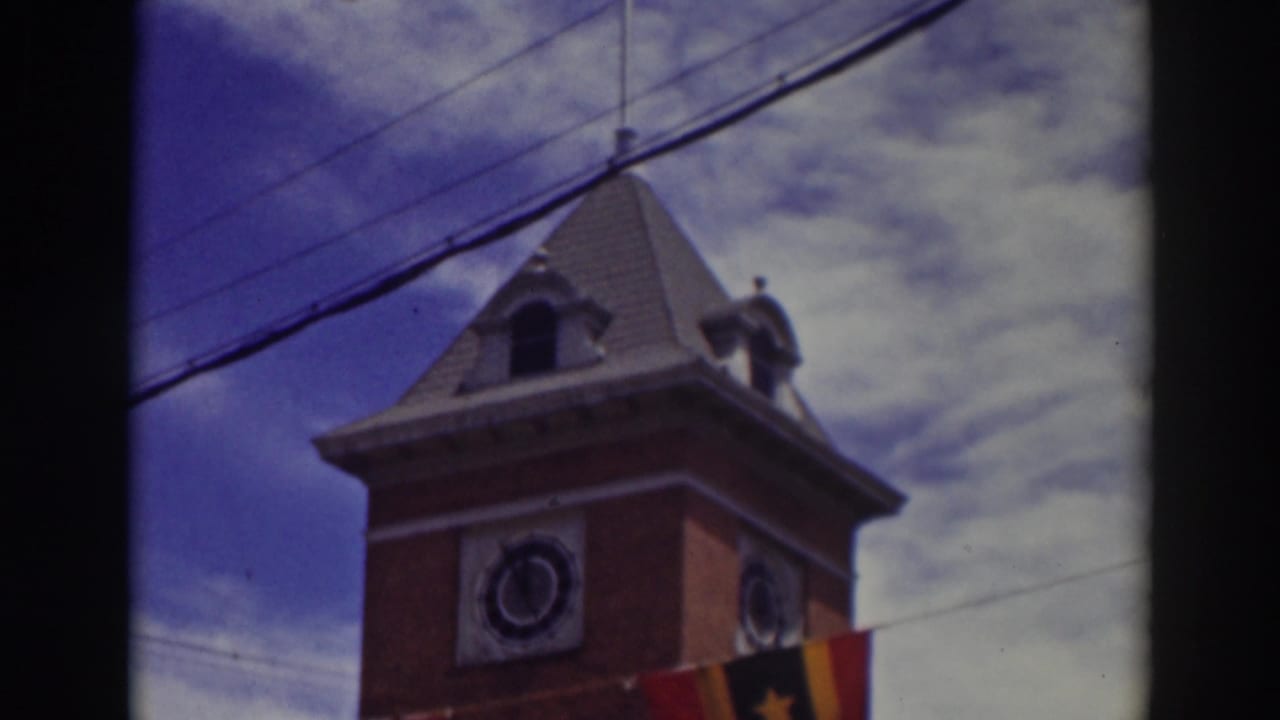 Brick clock tower under blue sky with overhead wires and a partial flag at the lower edge.