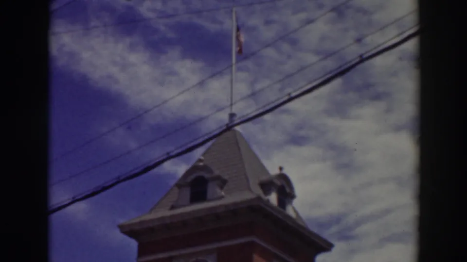 1937 Truckee frame showing the upper clock tower, flagpole, and crossing wires, with home-movie softness and color fading.