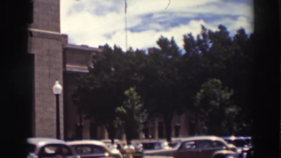 Truckee, California street view from 1937 home-movie footage, with parked cars, trees, a globe streetlamp, and a brick building.
