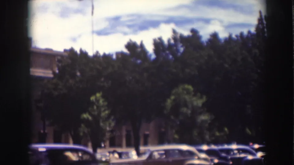 1937 Truckee street scene with dark tree canopy, parked automobiles, a brick facade, and visible 8mm film gate edges.