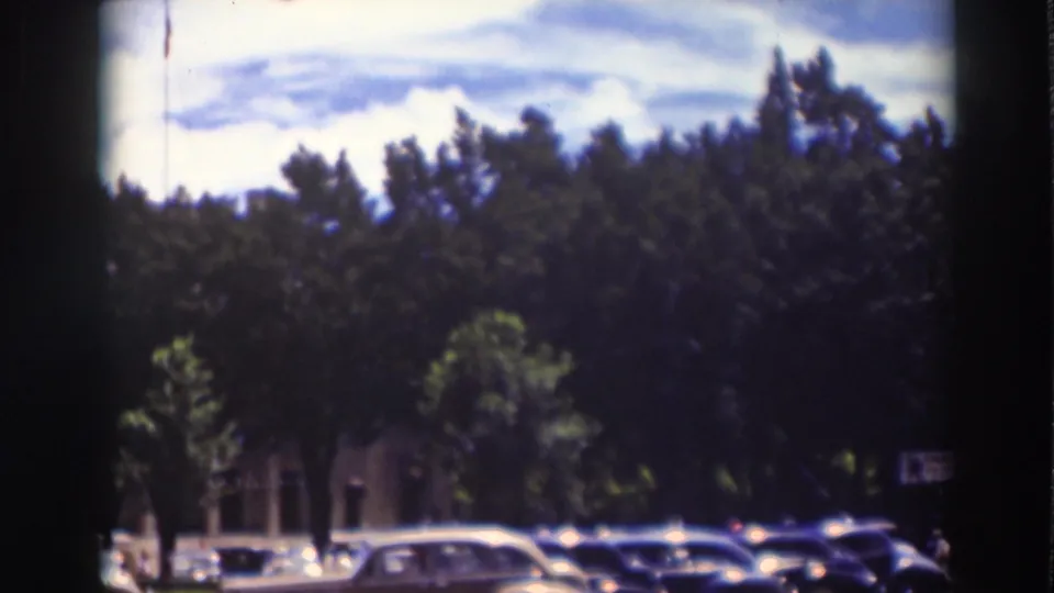 Truckee, California home-movie frame showing parked cars, dense street trees, brick building details, and small indistinct pedestrian figures.