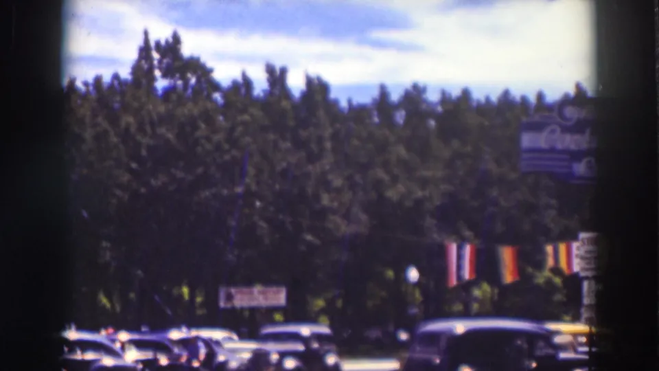Truckee, California street scene showing multiple 1930s cars, tall trees, hanging banners, and a partly readable roadside sign.