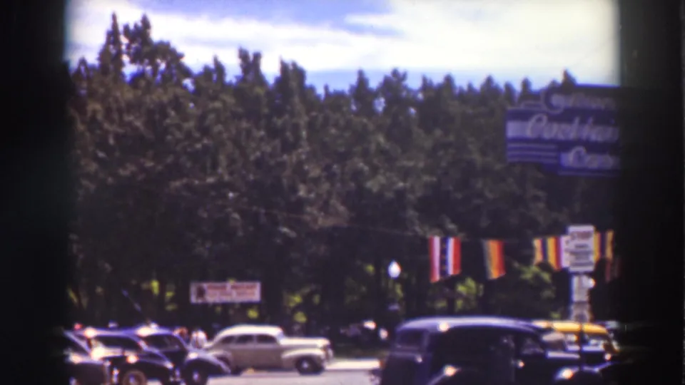 A bicyclist rides among 1930s street traffic in Truckee, with period cars, roadside signs, banners, and trees behind.
