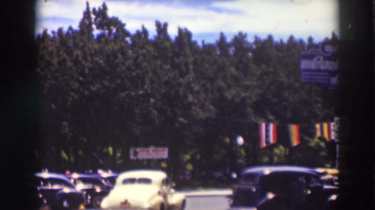 1937 Truckee street view with rounded automobiles, hanging flags, trees, and a partial Coca-Cola sign near the upper right.