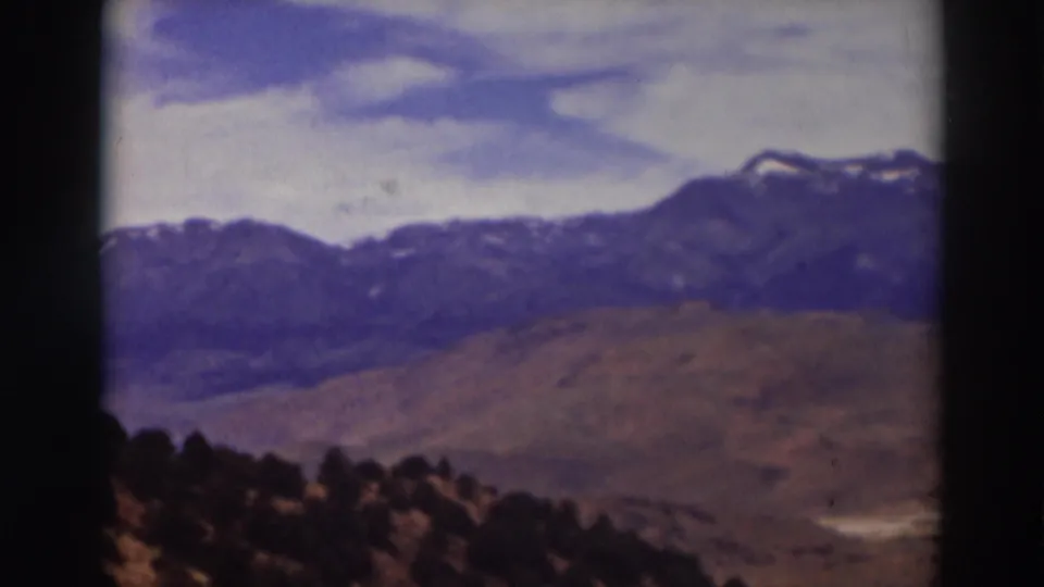 Truckee-area landscape frame showing blue-gray mountain ridges, tan hills, dark trees, and soft home-movie exposure.