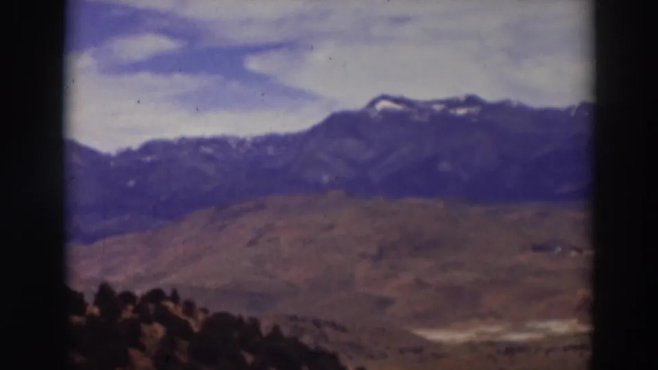 Truckee-area 8mm landscape frame with snow-marked peaks, brown hills, scattered clouds, and dark foreground vegetation.