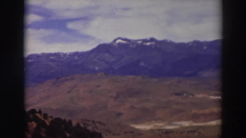 1937 Truckee, California home-movie frame showing a soft mountain panorama over dry terrain with dark trees in the foreground.