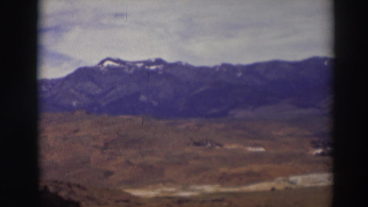 1937 Truckee-area home-movie view of open brown terrain below a distant mountain range with small snow patches and a cloudy sky.