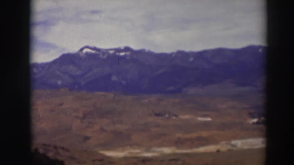 1937 Truckee-area home-movie view of open brown terrain below a distant mountain range with small snow patches and a cloudy sky.