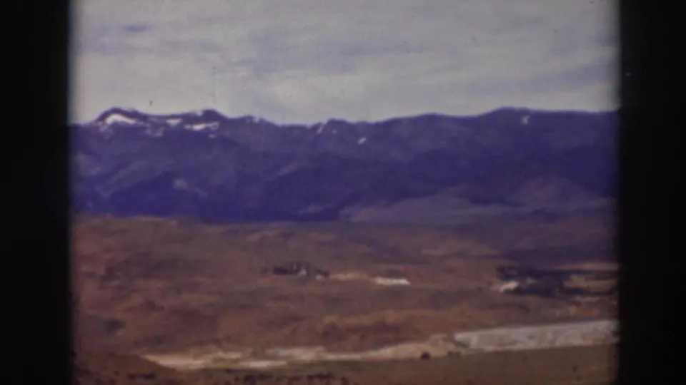 Truckee, California landscape frame showing dry rolling ground, a pale winding strip, and dark mountains under a muted sky.