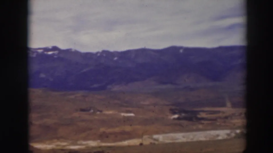 1937 home-movie frame from the Truckee area with open arid land leading to a dark mountain range beneath a pale sky.