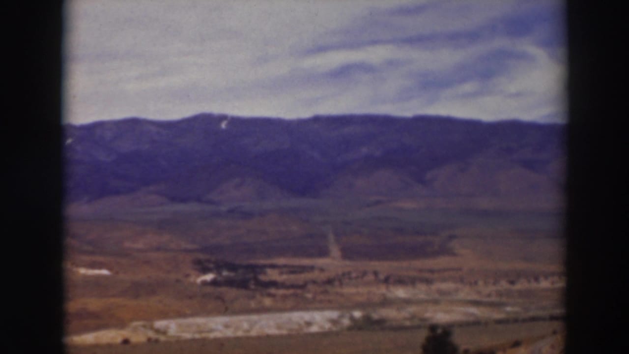 Wide valley with a dirt road, distant mountains, cloudy sky, and dark film-frame borders.