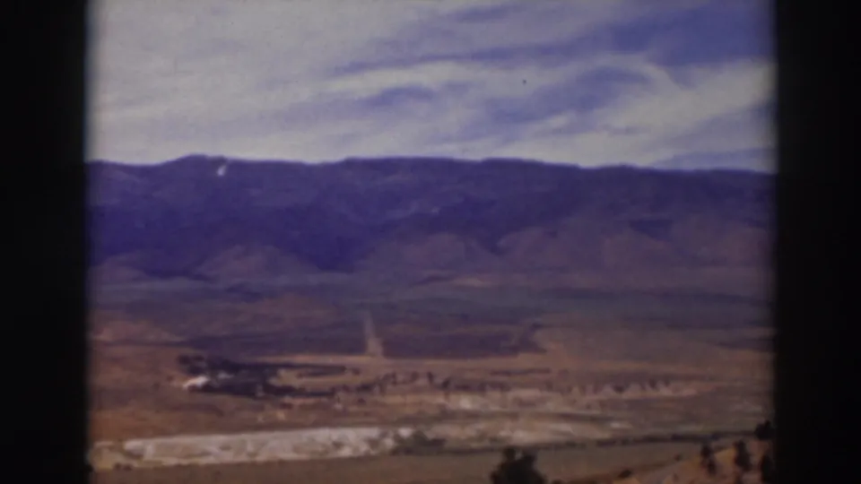 Truckee-area 1937 home-movie frame with a broad valley floor, faint road, low vegetation, and distant mountain ridge.