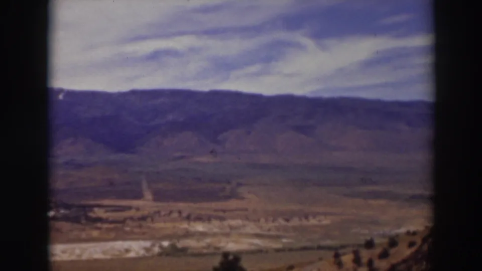 Wide 1937 Truckee landscape frame with soft 8mm color, showing dry ground, a road, hills, and clouds.