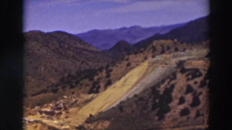 Truckee, California 1937 frame showing a pale winding road, scrubby slopes, and blue mountain ridges in soft 8mm color.