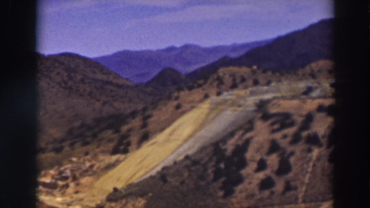 1937 8mm view near Truckee showing dry mountain slopes, a winding road, scattered brush, and distant ridgelines.
