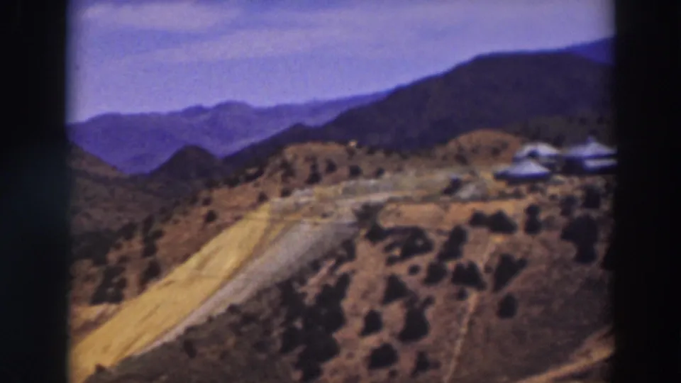 Truckee-area mountain view with an unpaved road, scrubby slopes, distant ridges, and small buildings at frame right.