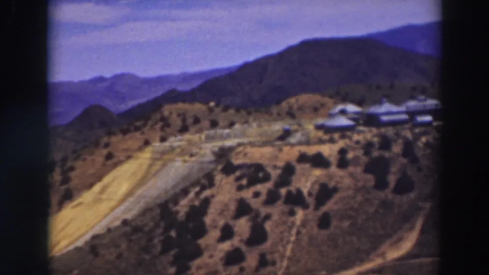 1937 home-movie frame near Truckee showing clustered mountain buildings beside a winding road and dry brush-covered hills.