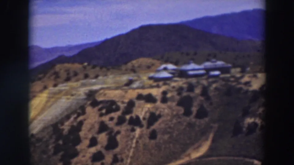 Truckee mountain landscape with low buildings on the slope, scrub vegetation, a curving road, and blue ridges in the distance.