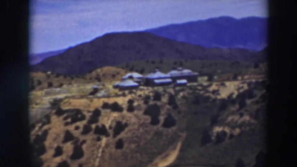 Truckee mountain landscape frame with pale buildings on a slope, scrubby vegetation, and layered ridges in the distance.