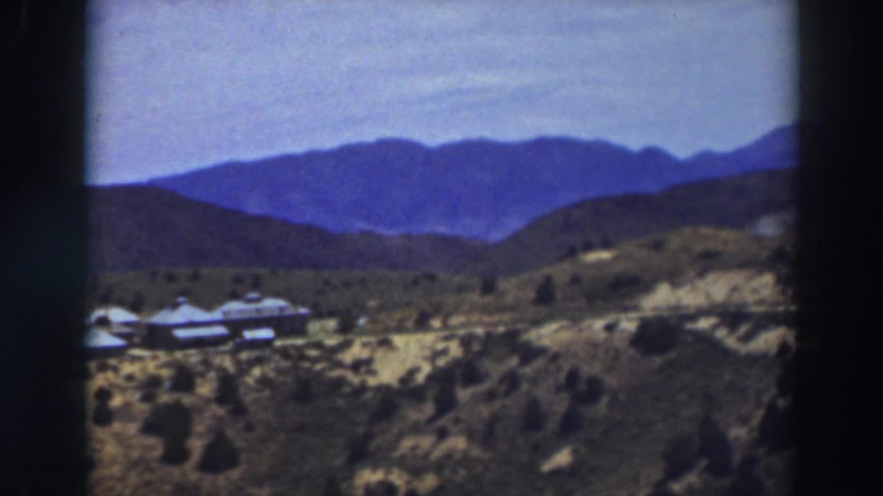 Distant blue mountains beyond scrubby hills and a small building cluster.