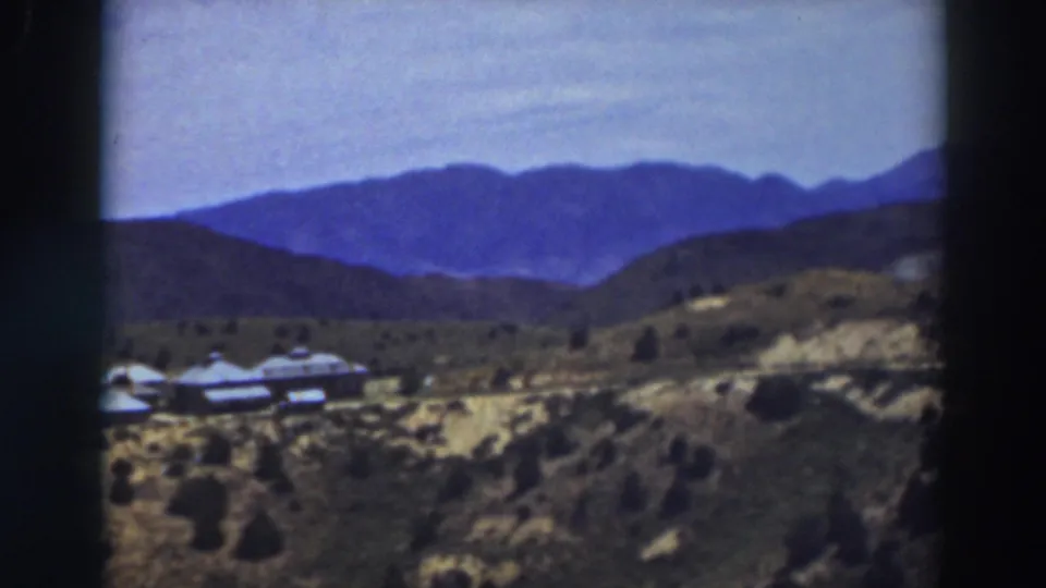 1937 Truckee-area home-movie frame showing distant mountains, open hills, sparse vegetation, and small buildings at left.