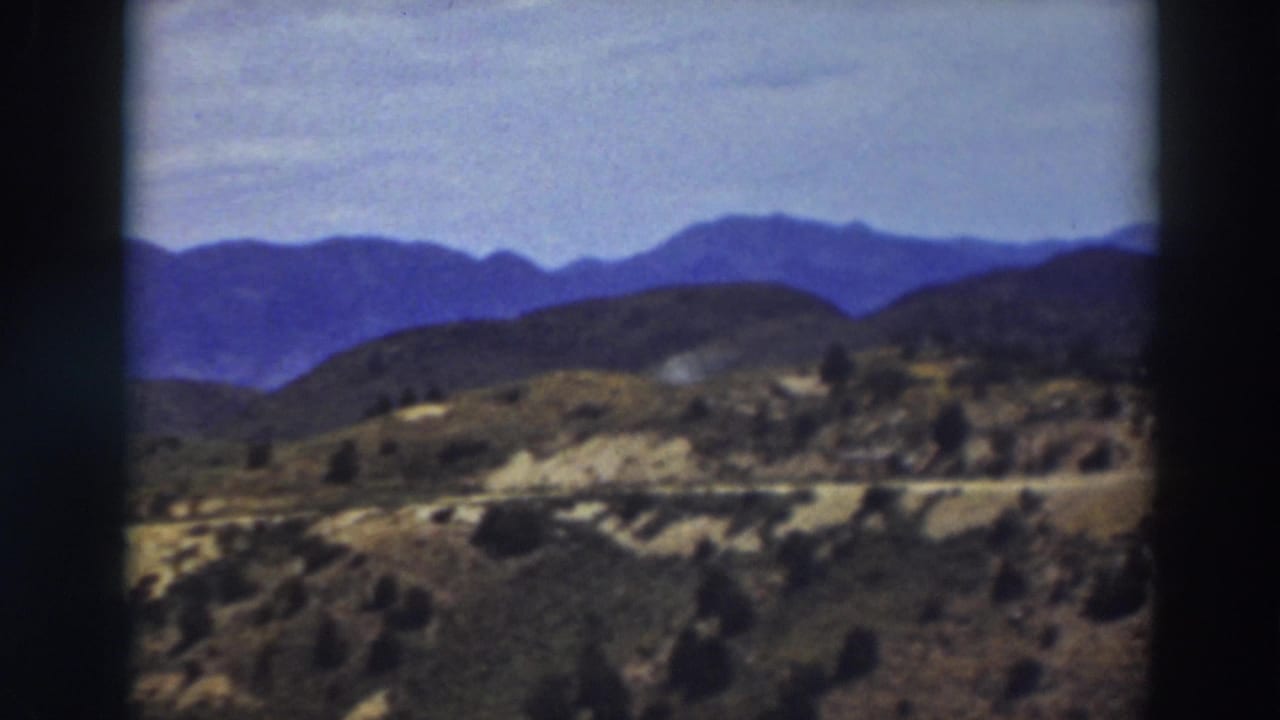 1937 8mm frame of the Truckee landscape, with soft blue ridges behind dry, brushy hills and a faint road line.