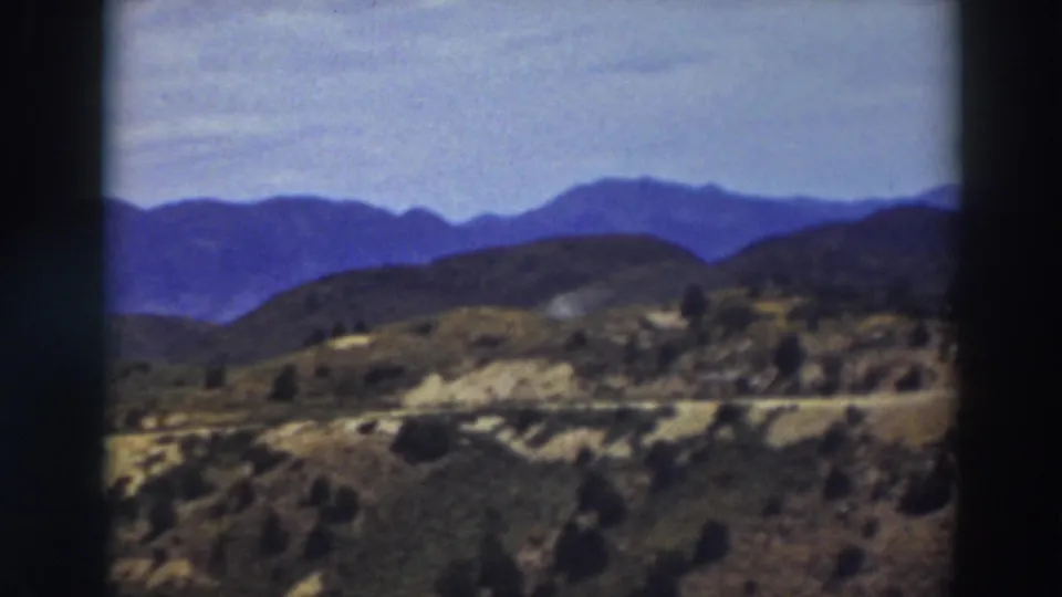 1937 8mm frame of the Truckee landscape, with soft blue ridges behind dry, brushy hills and a faint road line.