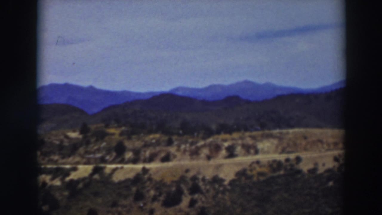 Distant blue mountains beyond dry hills, trees, and a pale sky.