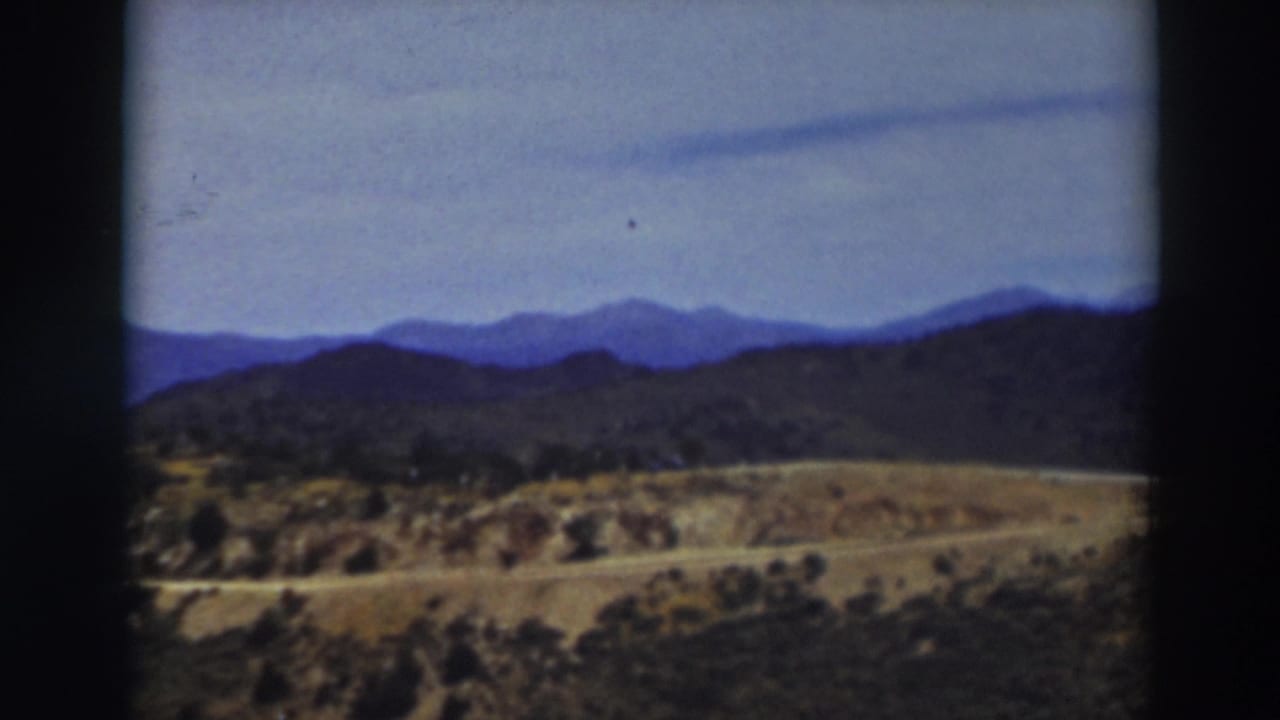 1937 8mm view near Truckee with a dirt road crossing dry hills below layered mountain ridges.