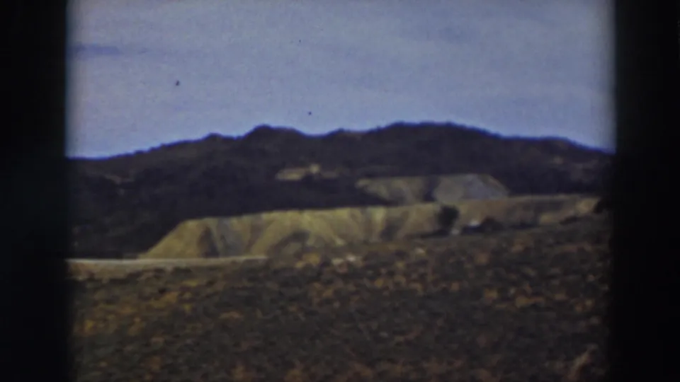 Truckee-area 8mm frame showing a darker ridgeline above pale eroded slopes and scrubby foreground terrain.
