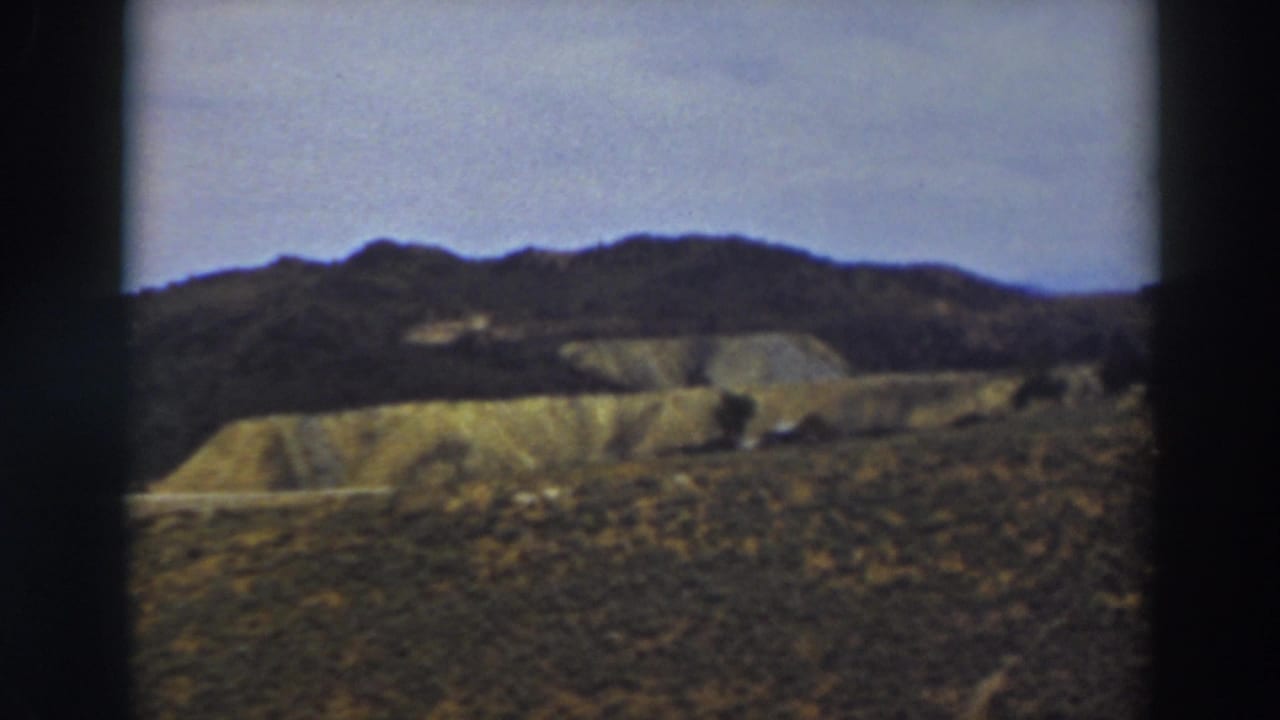 Rolling dry hills under a pale sky, seen through dark film gate edges.