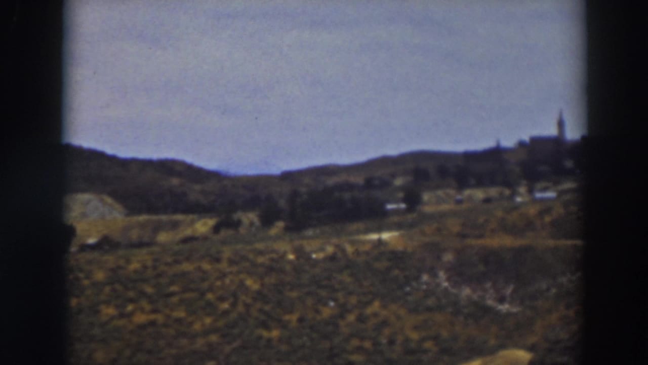 1937 Truckee landscape frame with open grassland, distant hillside buildings, and a steeple-like vertical structure at right.
