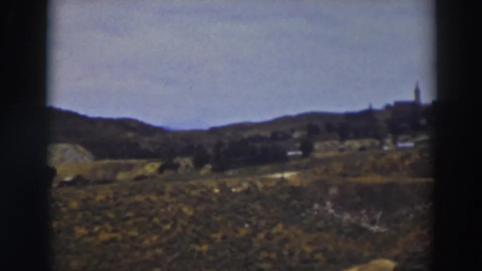 1937 Truckee landscape frame with open grassland, distant hillside buildings, and a steeple-like vertical structure at right.