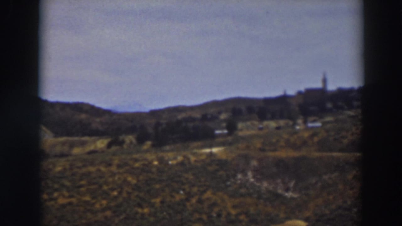 Distant hillside settlement with a church steeple beyond scrubby foreground slopes.