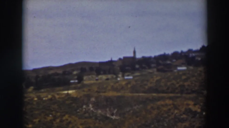 1937 Truckee countryside frame showing brushy slopes, small distant structures, and a steeple on the horizon line.