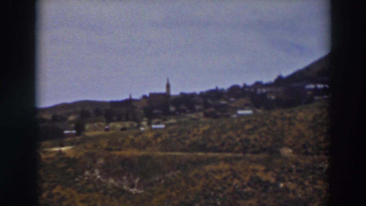 Truckee-area 8mm frame with open hillside, scattered distant structures, and a steeple silhouetted against the pale sky.