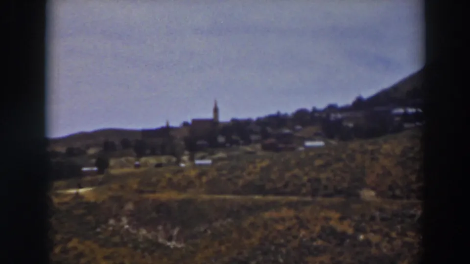 Truckee-area 8mm frame with open hillside, scattered distant structures, and a steeple silhouetted against the pale sky.