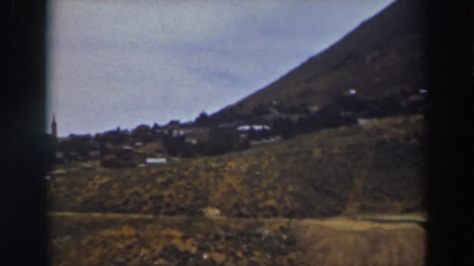 Final 8mm frame of the Truckee hillside town view, with dry terrain, low buildings, and a partial steeple near the left edge.