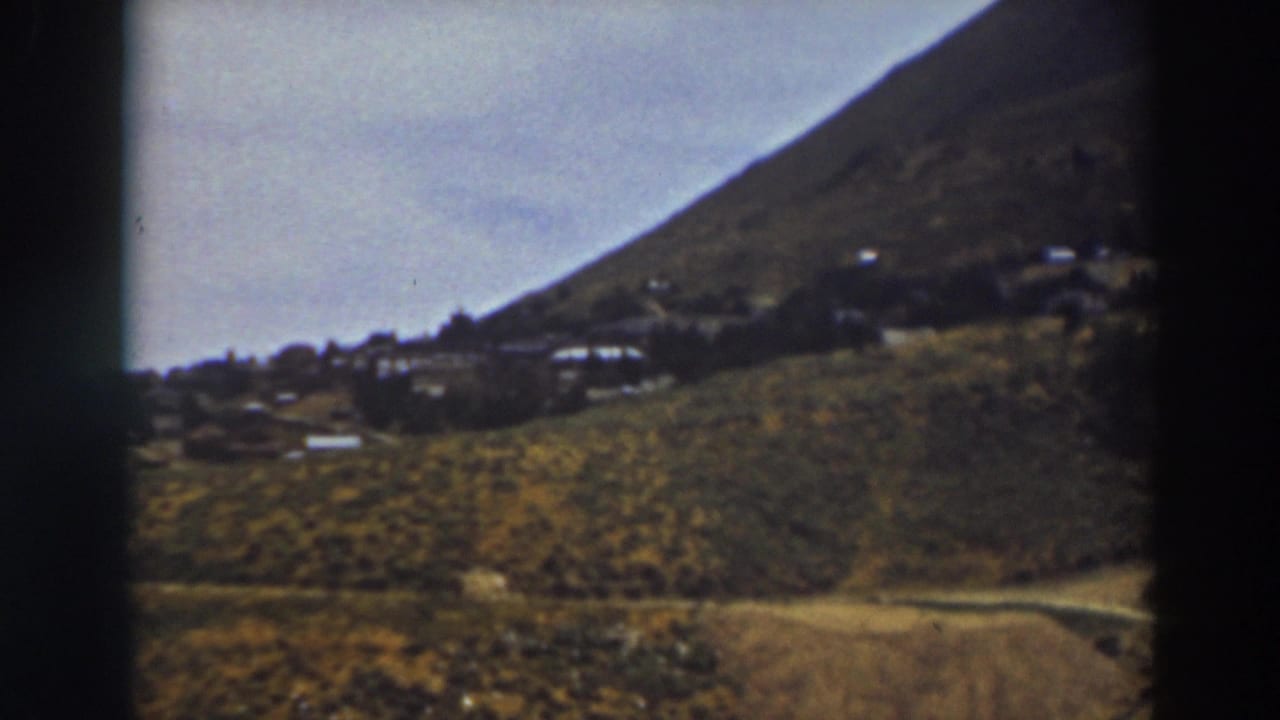 Distant hillside settlement below a sloping mountain with fields in the foreground.