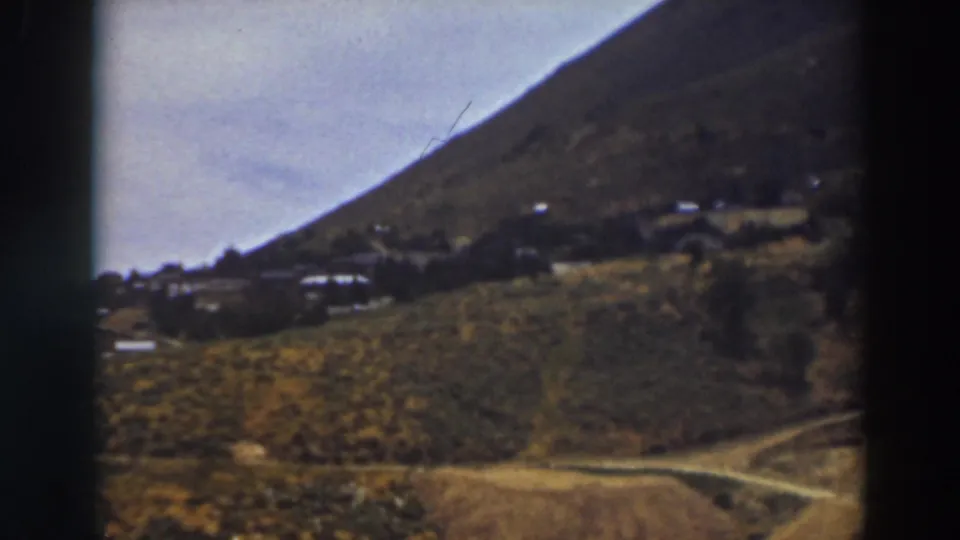 1937 Truckee view with a dirt road crossing open terrain, scattered hillside structures, scrub vegetation, and a dark 8mm frame border.